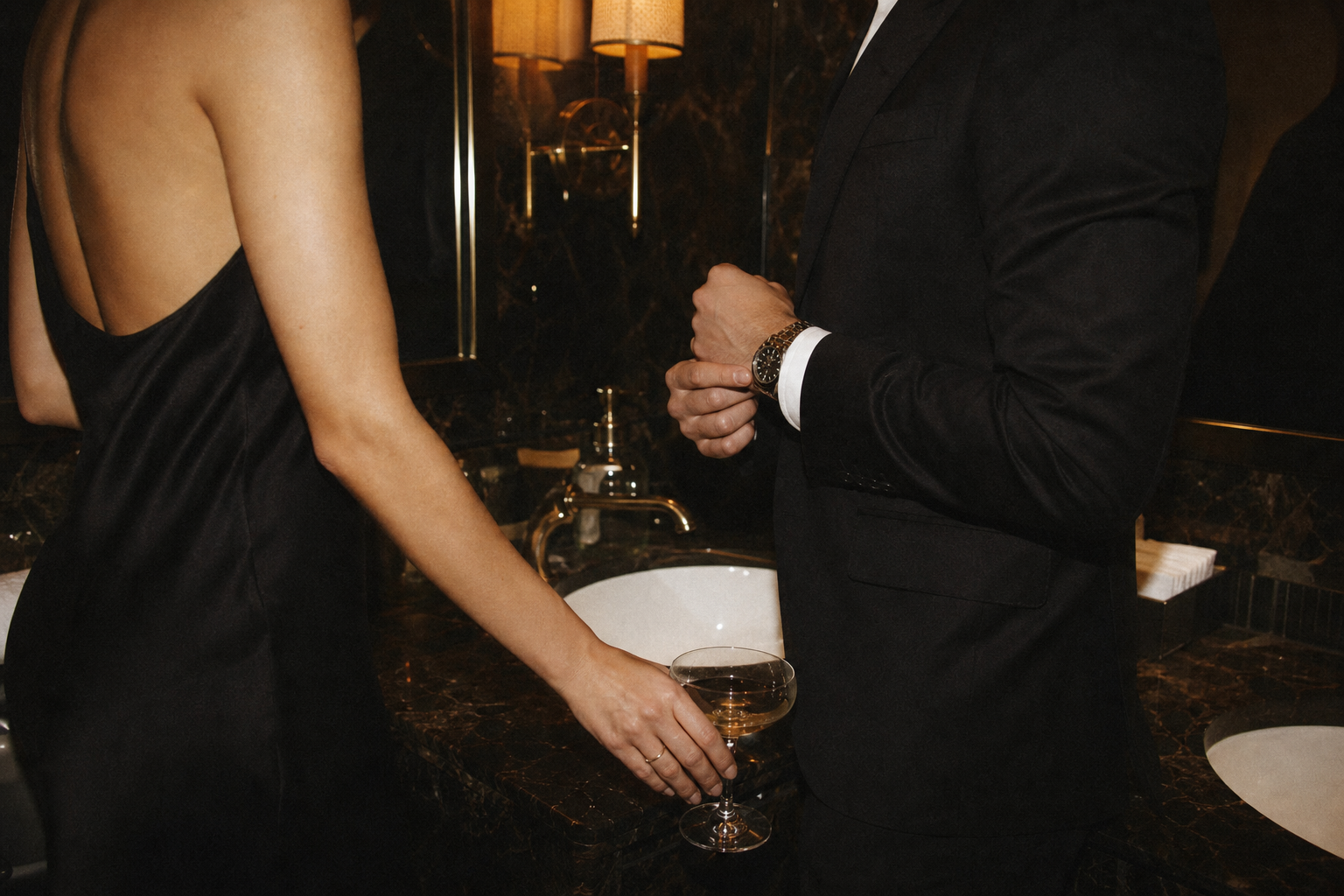Couple pausing at a hotel powder-room mirror before returning to a candlelit party.